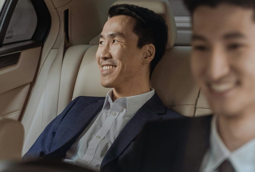 Two men in formalwear enjoying a comfortable ride in a luxury car, smiling.